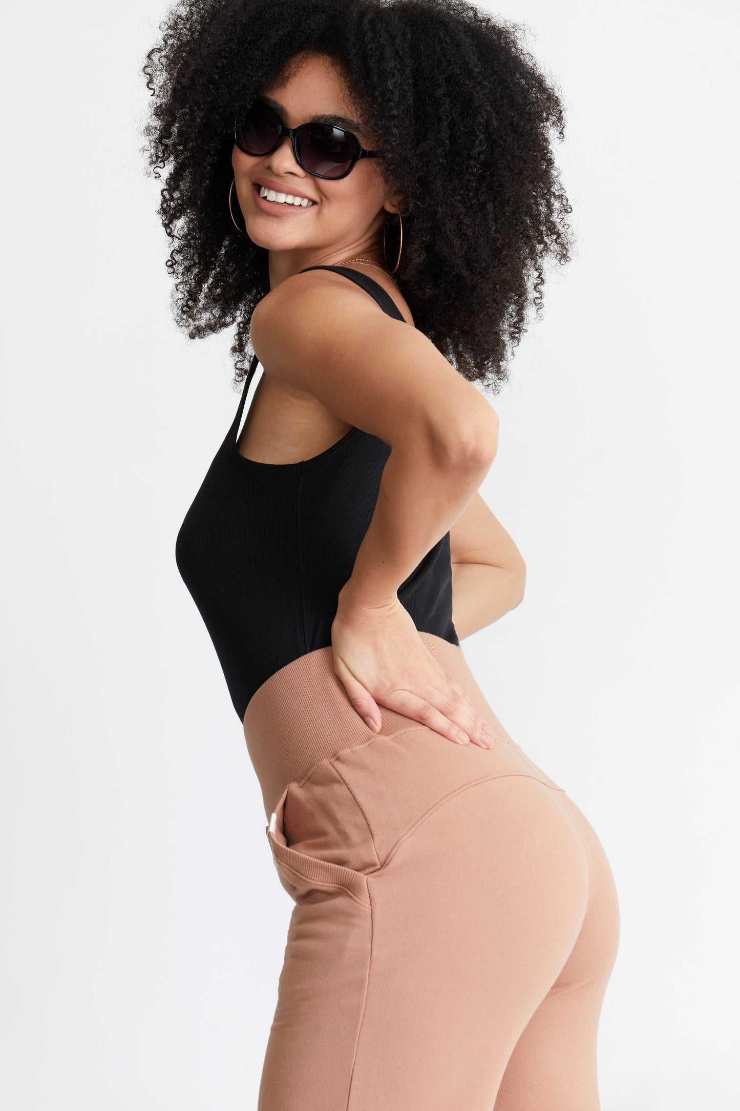 Woman wearing a black sports bra and beige leggings on a white background