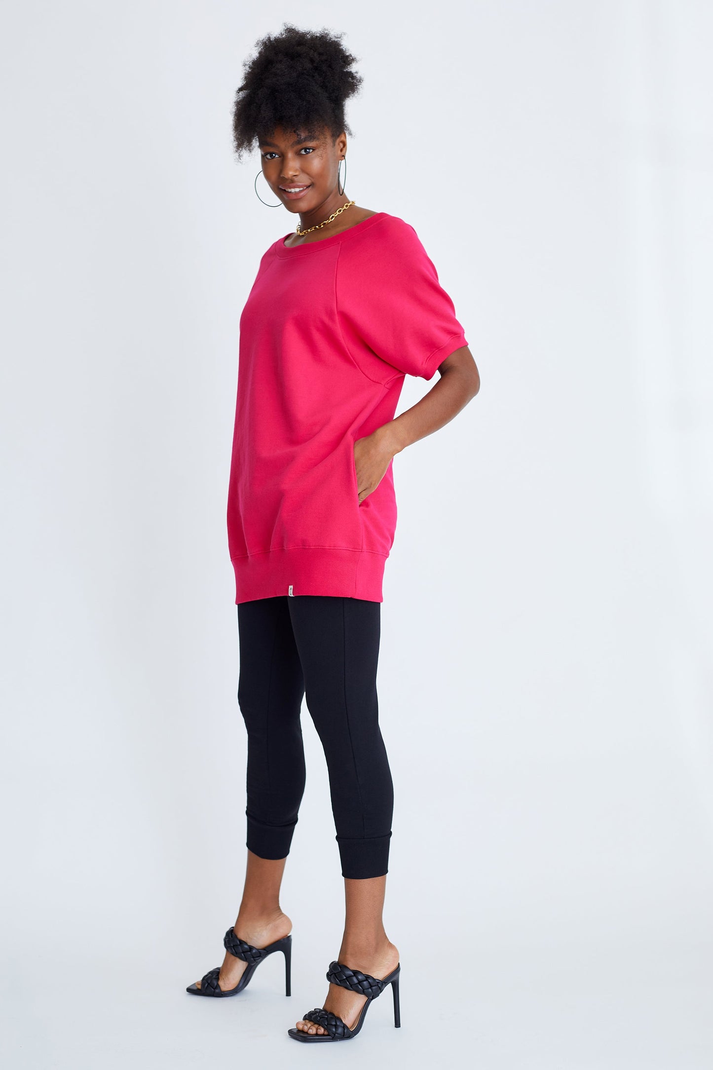 Woman wearing a bright pink oversized sweater and black leggings on a white background